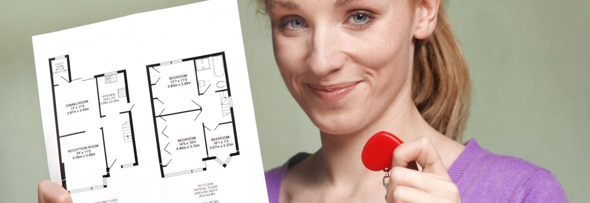 A woman holds a key in one hand and a printed copy of floor plans in the other