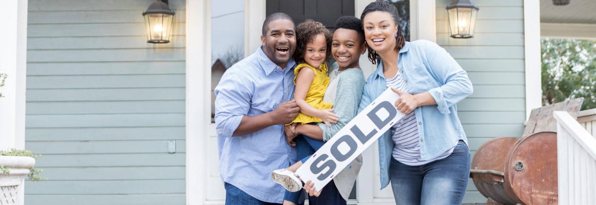 family on front porch of house holding sold sign