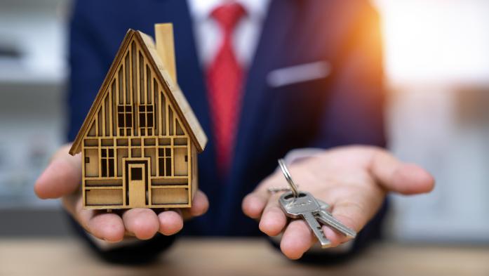 Blurry man in suit holds small house and keys in his hands