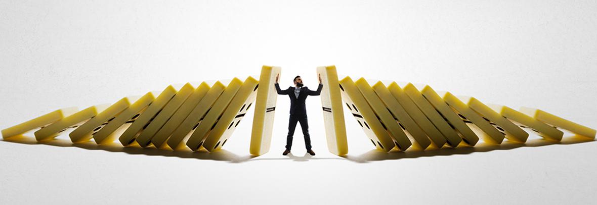 Business man standing in the middle of two sets of dominoes falling with man stopping the falling