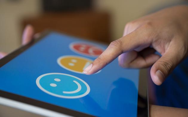 Finger choosing between smiling, neutral and negative faces on an iPad