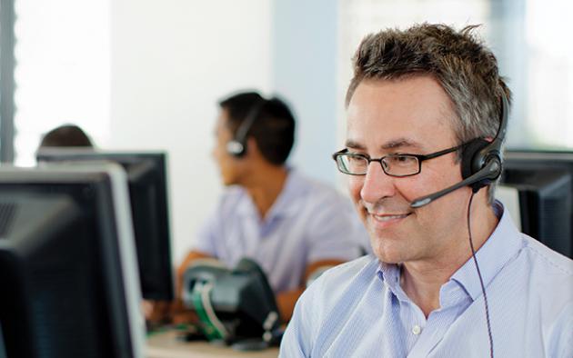 photo of a male tech support person with a headset on in front of a computer