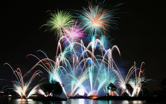 Multiple fireworks exploding above a lake