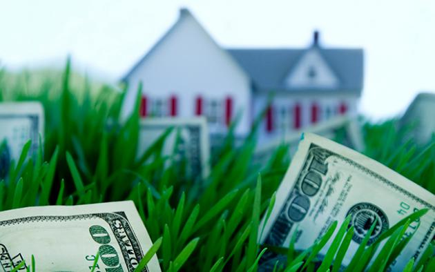 Photo illustration of a house nestled in grass and money
