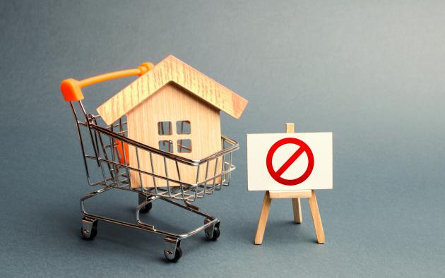 Wood replica of a house inside a shopping cart with a "no" symbol beside it on an easel