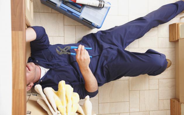 plumber with tools on floor with head under cabinet