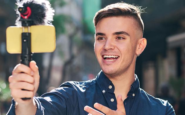 Photo of a young man holding his smartphone on a tripod taking video of himself