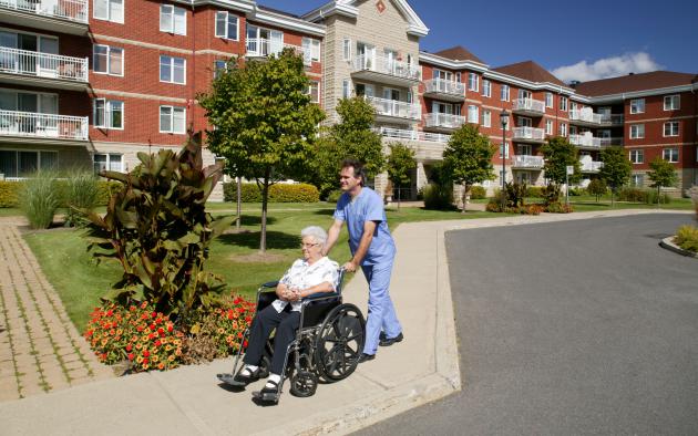 Nurse pushes an older woman in a wheelchair in front of a senior living home