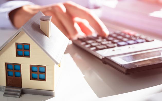Photo of a persons hand using a calculator and a small house in the foreground