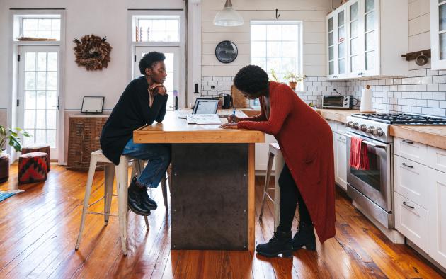 Woman signing paperwork in kitchen with another woman