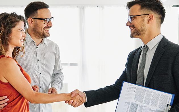 Photo of male realtor shaking the hands of a couple/clients