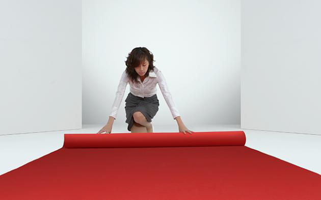 business woman rolling out a red carpet in a white room