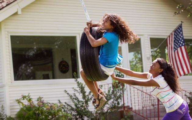 Kids playing on tire swing in front yard of house