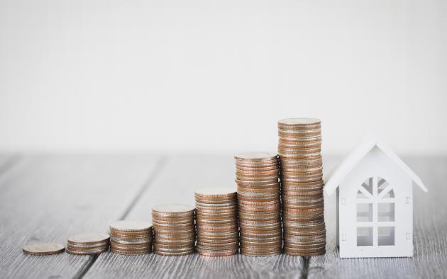 Small paper house with coins stacked up beside it