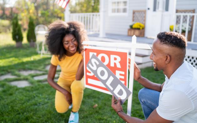 Husband and wife showing off sold sign in front of house