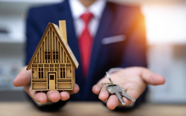 Blurry man in suit holds small house and keys in his hands