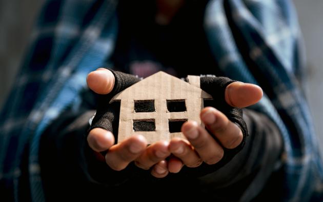 Homeless man holds cardboard cutout of a house