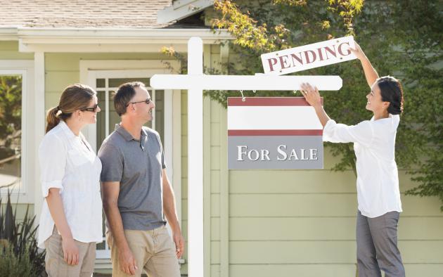 Couple watches their Realtor add a pending sign to a home's for-sale sign