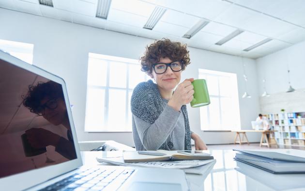 woman at computer desk holding coffee cup