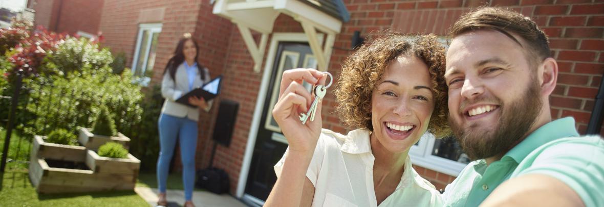 a young couple celebrate getting the keys to their new home by taking a selfie in the garden