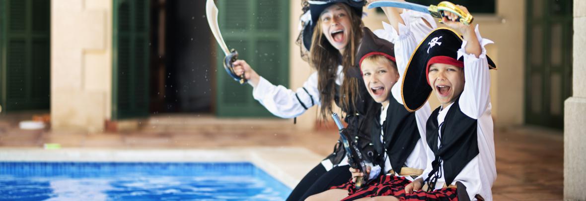 Three kids dresses as pirates dip their feet in a swimming pool