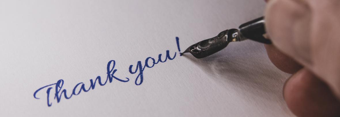 A hand with an ink pen is writing thank you