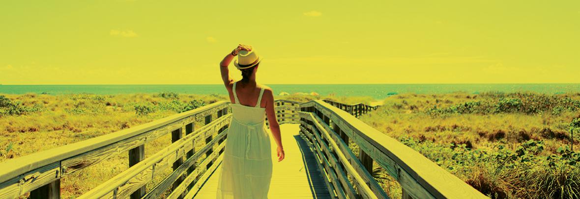 Photo of woman on a boardwalk walking towards the beach