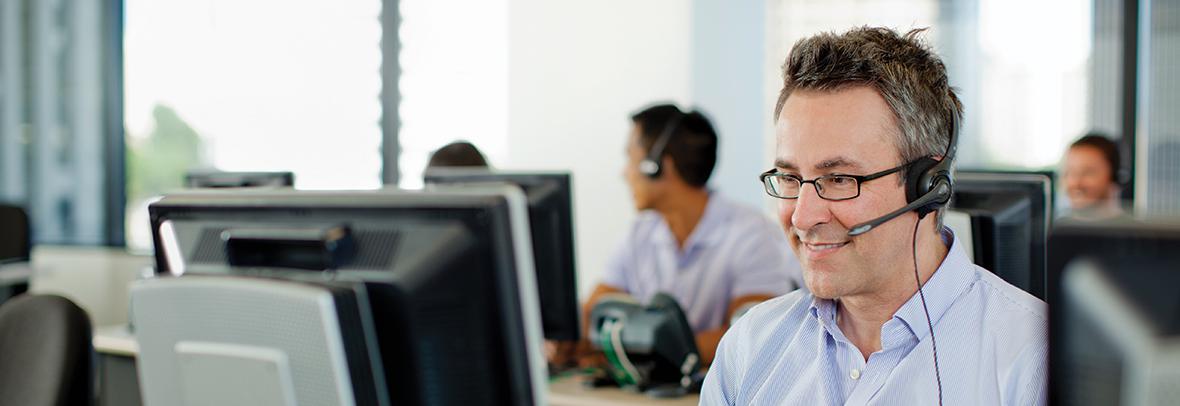 photo of a male tech support person with a headset on in front of a computer