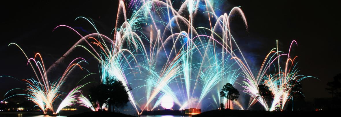 Multiple fireworks exploding above a lake