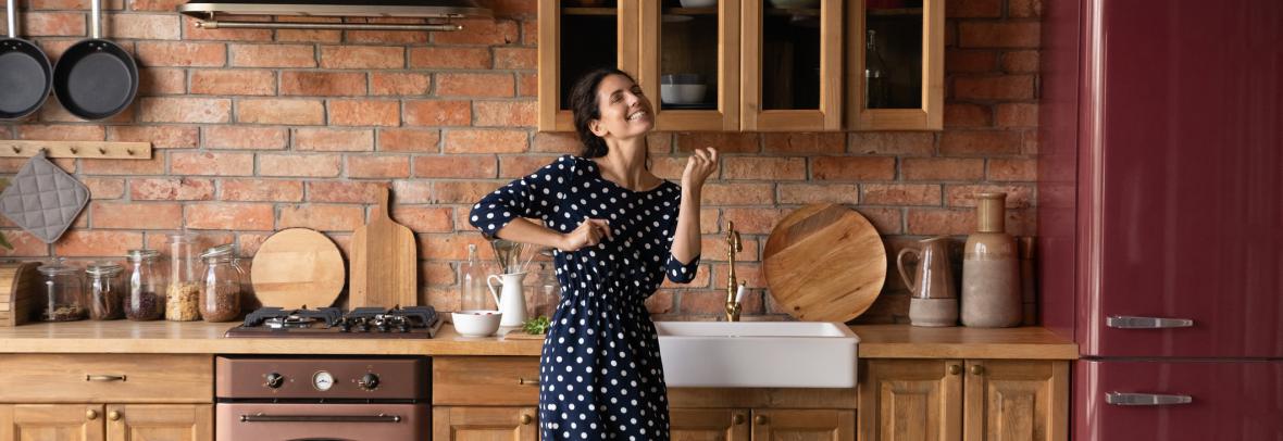 Woman dancing in a kitchen with wood cabinets and dark red appliances