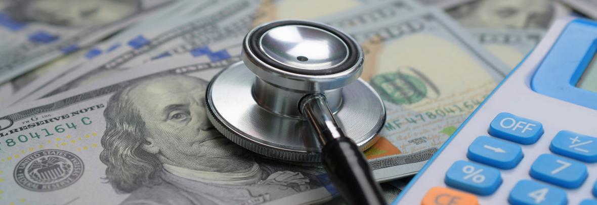 A Stethoscope and calculator on a pile of hundred dollar bills