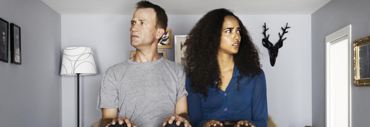 A confused couple sit in a tiny couch inside a tiny home