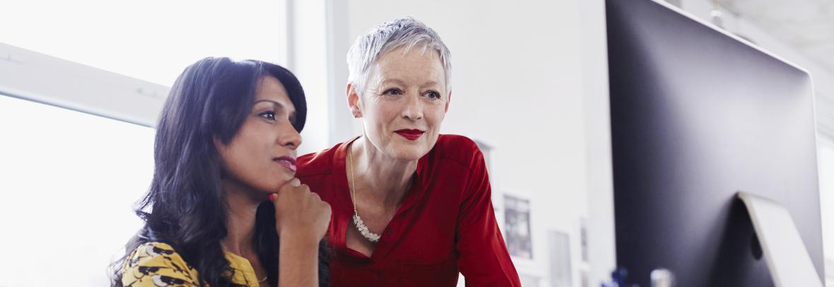 Mature woman mentoring younger woman at computer in business setting