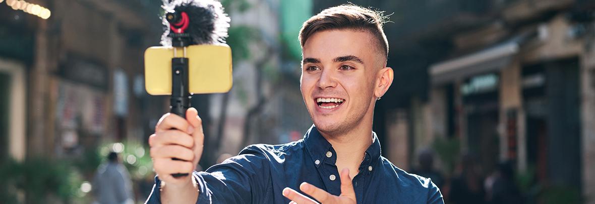 Photo of a young man holding his smartphone on a tripod taking video of himself