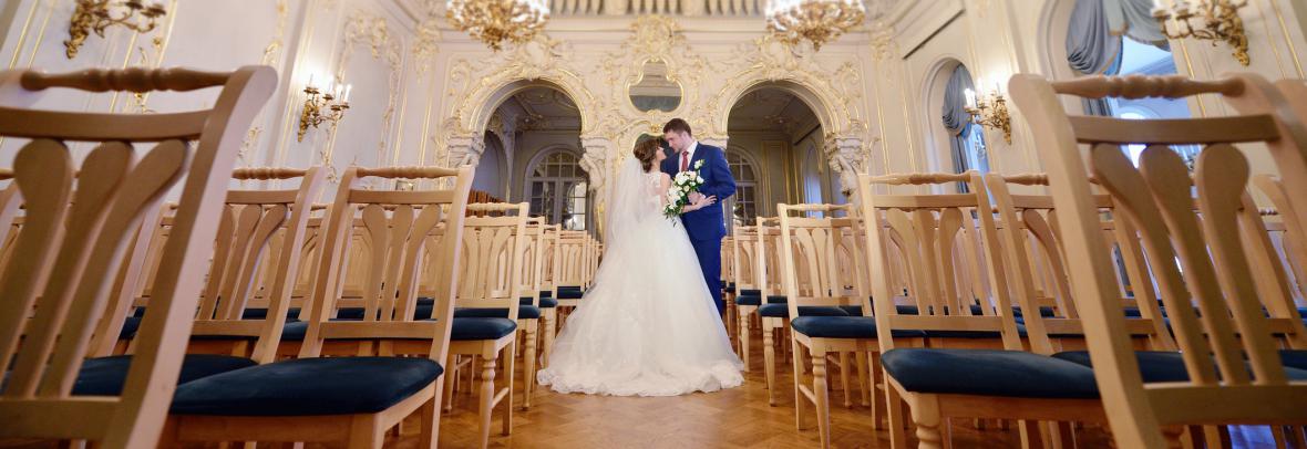 A bride and groom embrace in the aisle of a lavish church