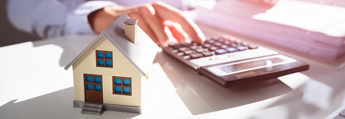 Photo of a persons hand using a calculator and a small house in the foreground