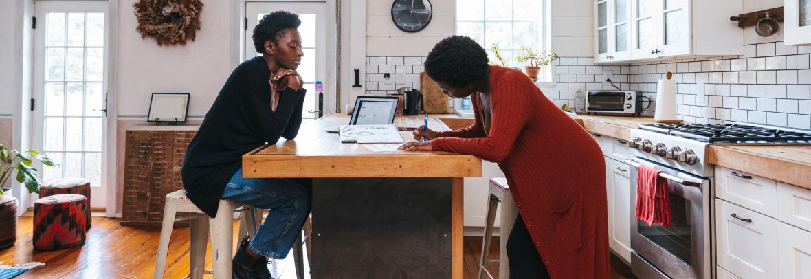 Woman signing paperwork in kitchen with another woman