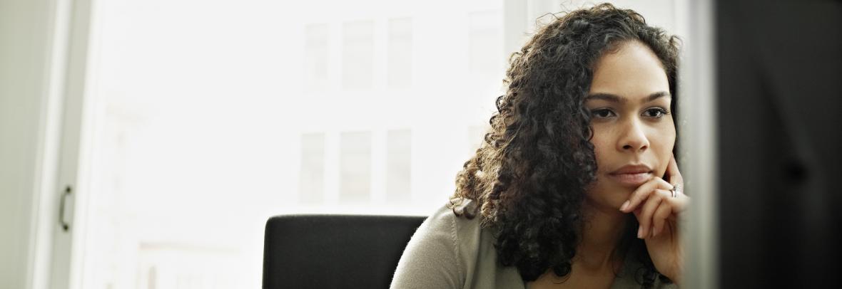 woman with hand to face in front of computer monitor