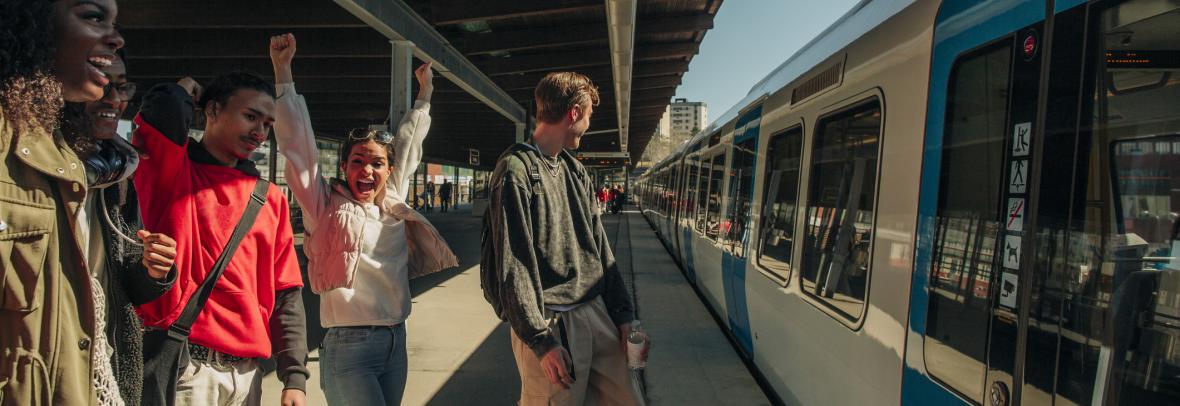 Four people cheer the arrival of a train in a local train station