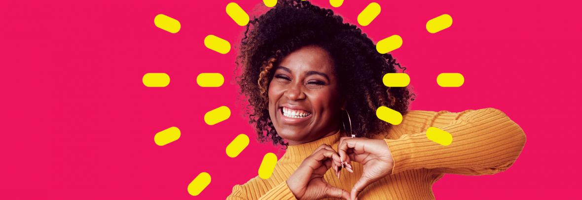 African American woman making a heart shape with hands on magenta background
