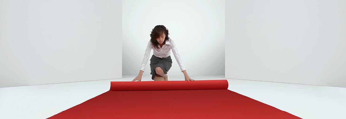 business woman rolling out a red carpet in a white room