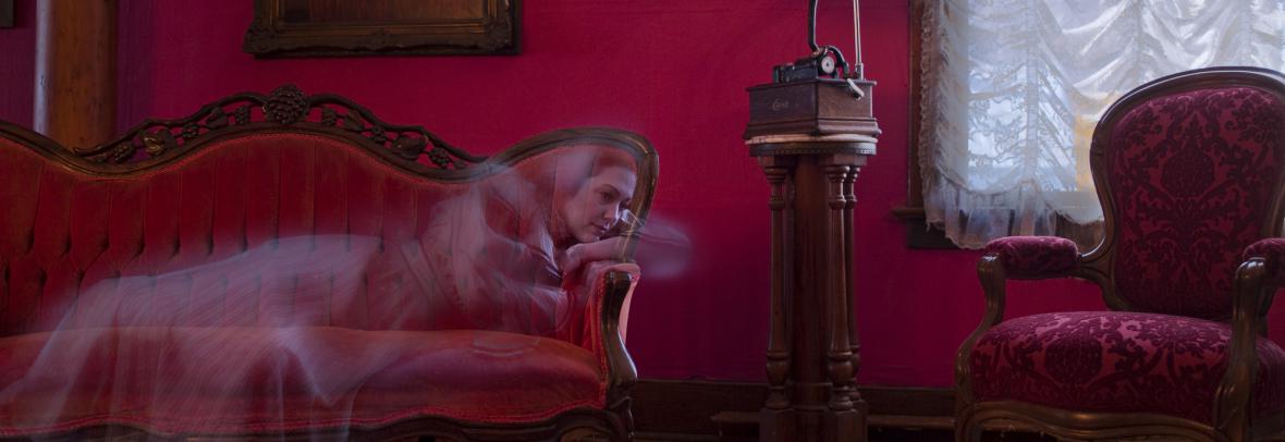 Woman's ghost lies on a red couch in a red old-fashioned room