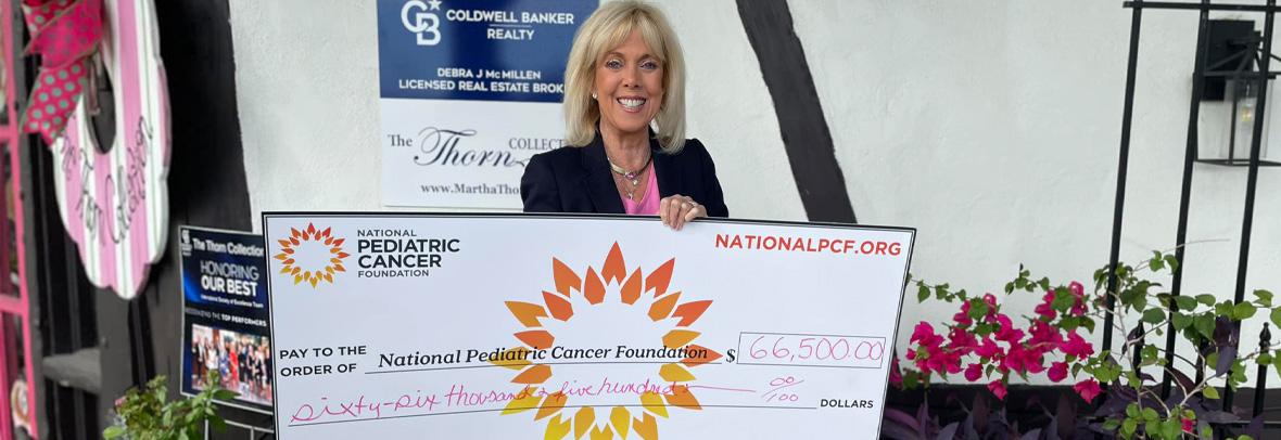 Martha Thorn holds a large version of a $66.5K check for pediatric cancer research