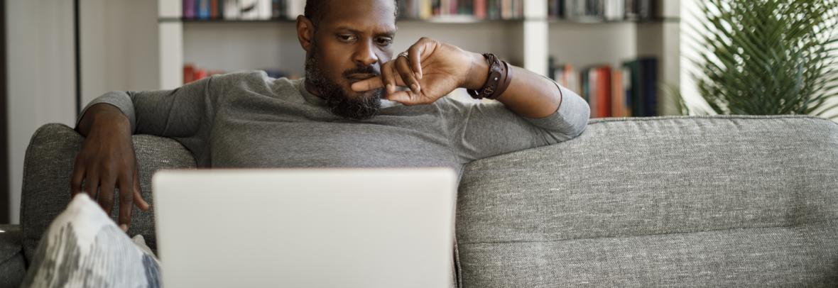 man who appears concerned looking at laptop while sitting on couch