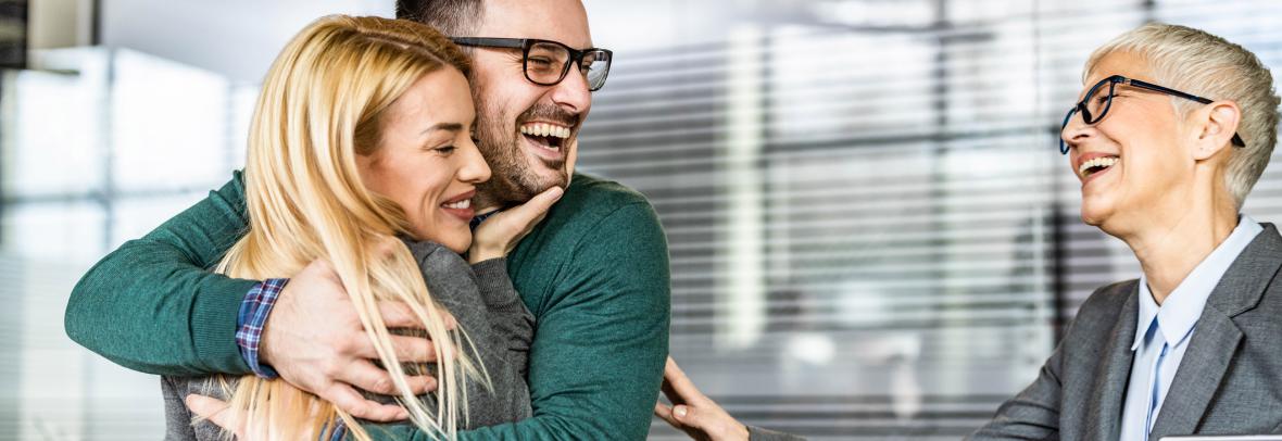 couple hugging and smiling while older woman looks on, smiling.