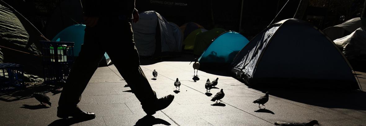 man's legs shown walking past homeless tents