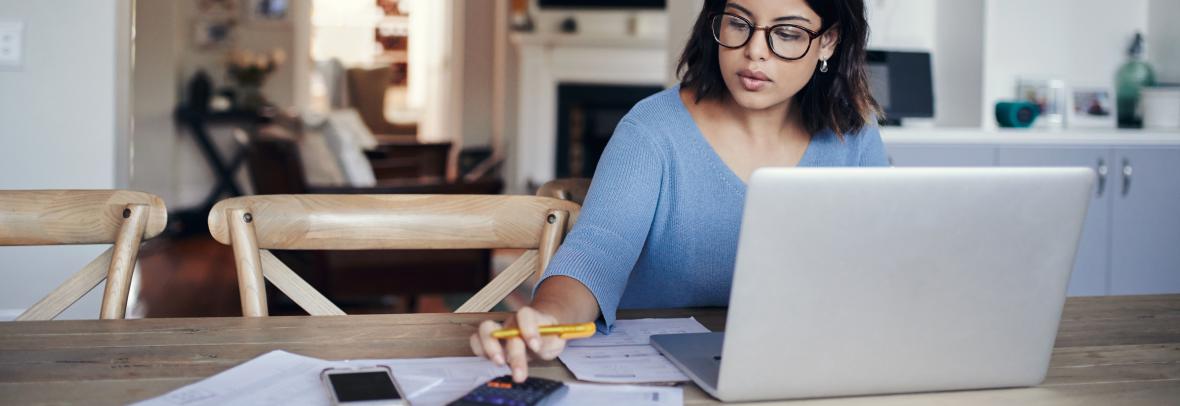 woman using laptop and calculator at kitchen table