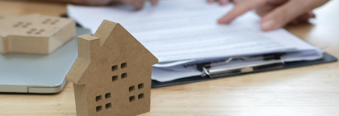 small cardboard house on desk with hands filling out paperwork