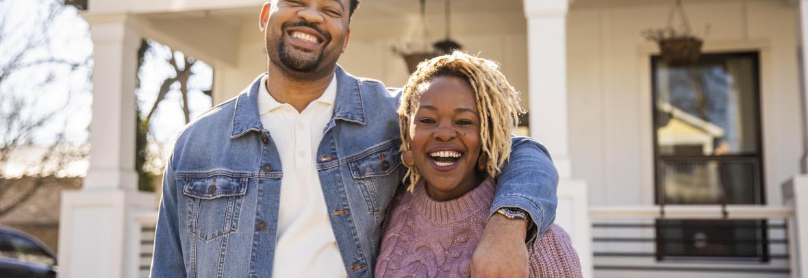 black couple smiling in front of a home 