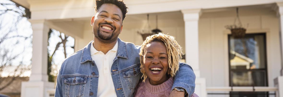 black couple smiling in front of a home 